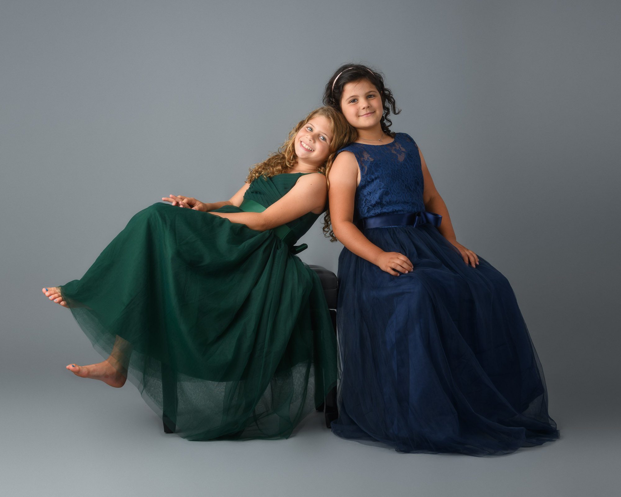 Two young girls in flowing green and navy dresses pose together during a studio family portrait session, showcasing the clean, timeless style that DC family photographer Lisa Maco is known for.