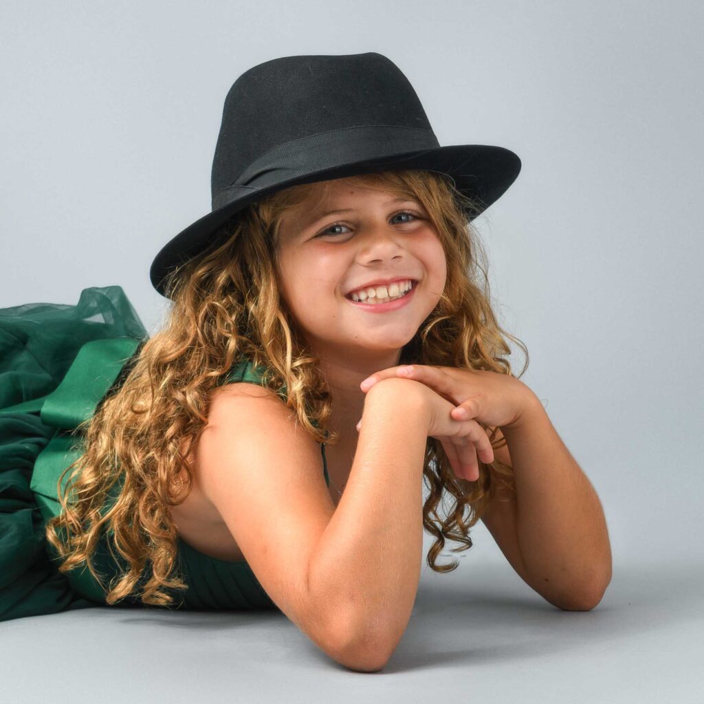 Smiling tween girl in a black hat and green shirt poses for a classic studio portrait