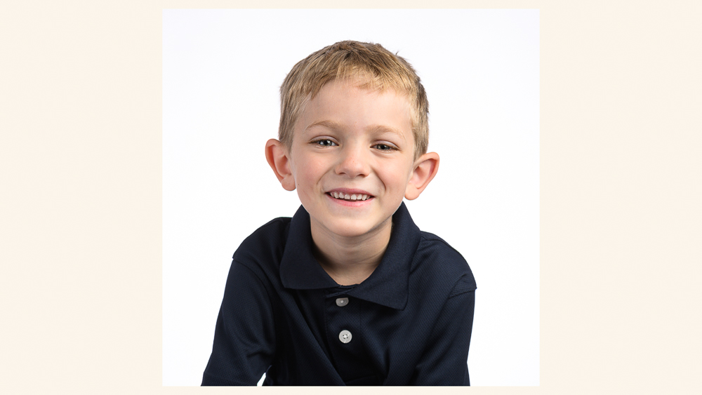 Young boy with blonde hair smiling at camera wearing a dark navy polo shirt | Lisa Maco Photography
