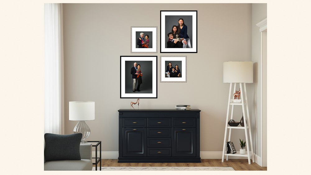 Four framed family portraits arranged on a beige wall above a dark navy dresser in a modern living room setting | Lisa Maco Photography