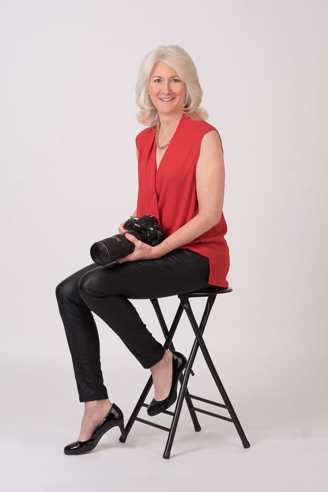 Professional DC family photographer Lisa Maco poses with her camera on the About page, showcasing her approachable style for creating classic studio portraits