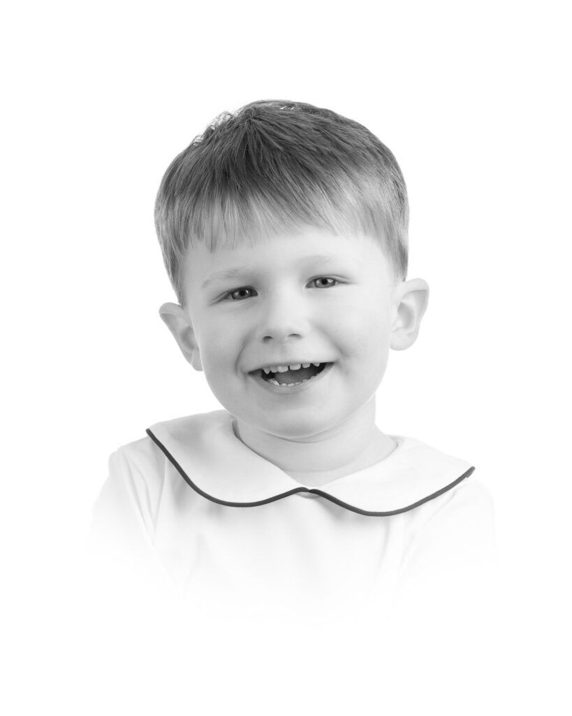 Young boy with a bright smile wearing a white shirt with dark trim in a classic studio portrait by a DC family photographer