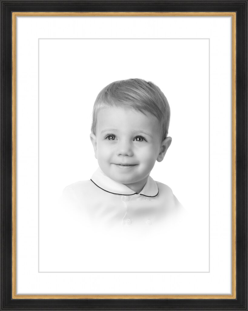 Young boy in a classic black and white heirloom portrait, smiling gently while wearing a collared shirt in a timeless vignette-style photograph framed for display