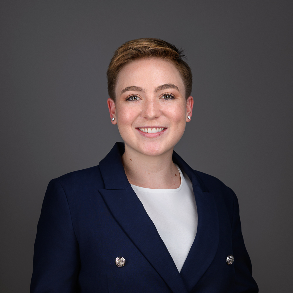 Professional headshot of a smiling woman with short reddish-brown hair wearing a navy blazer