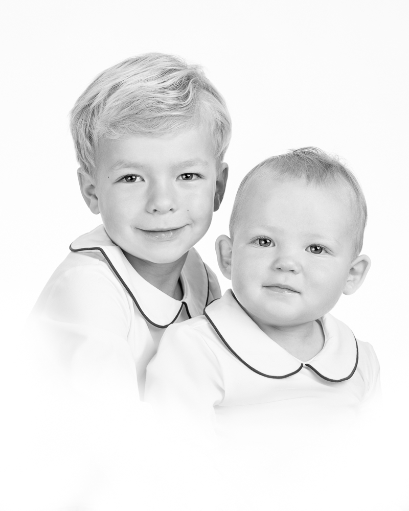 Two young boys in matching white shirts with navy trim pose together for a classic family portrait session with a DC photographer