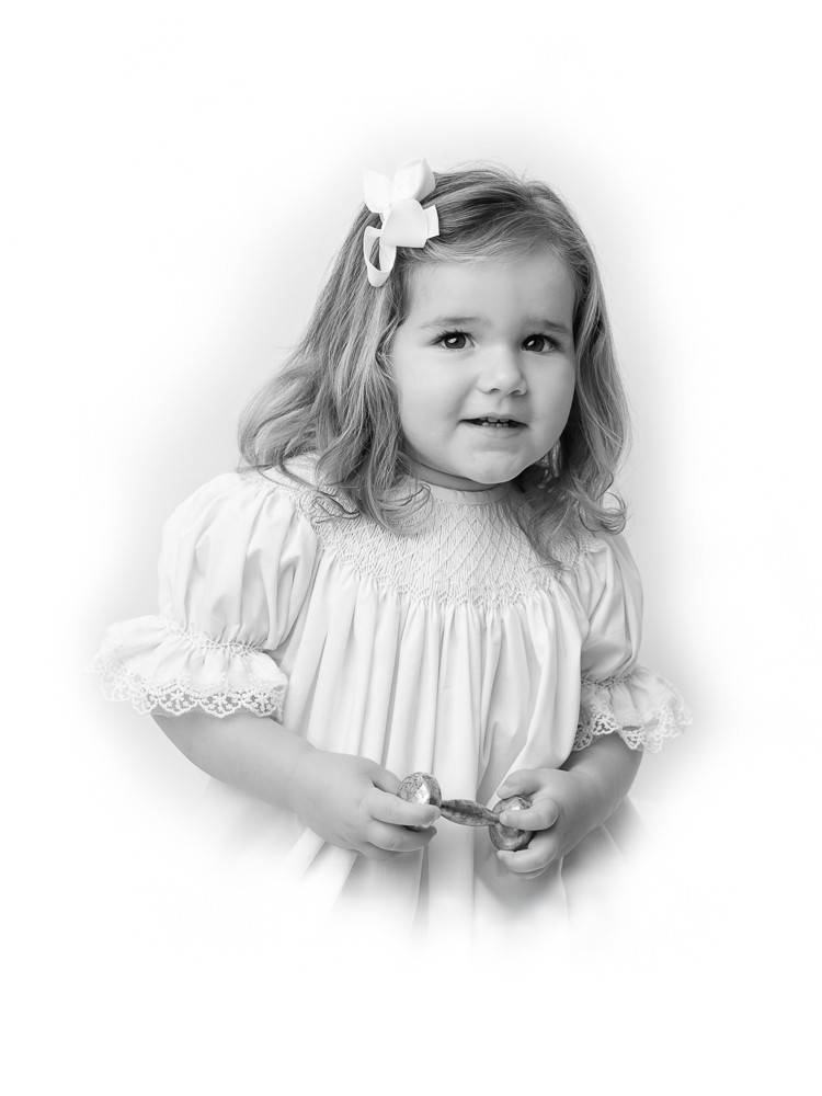 Young girl in a white dress with lace trim and hair bow during a classic studio portrait session