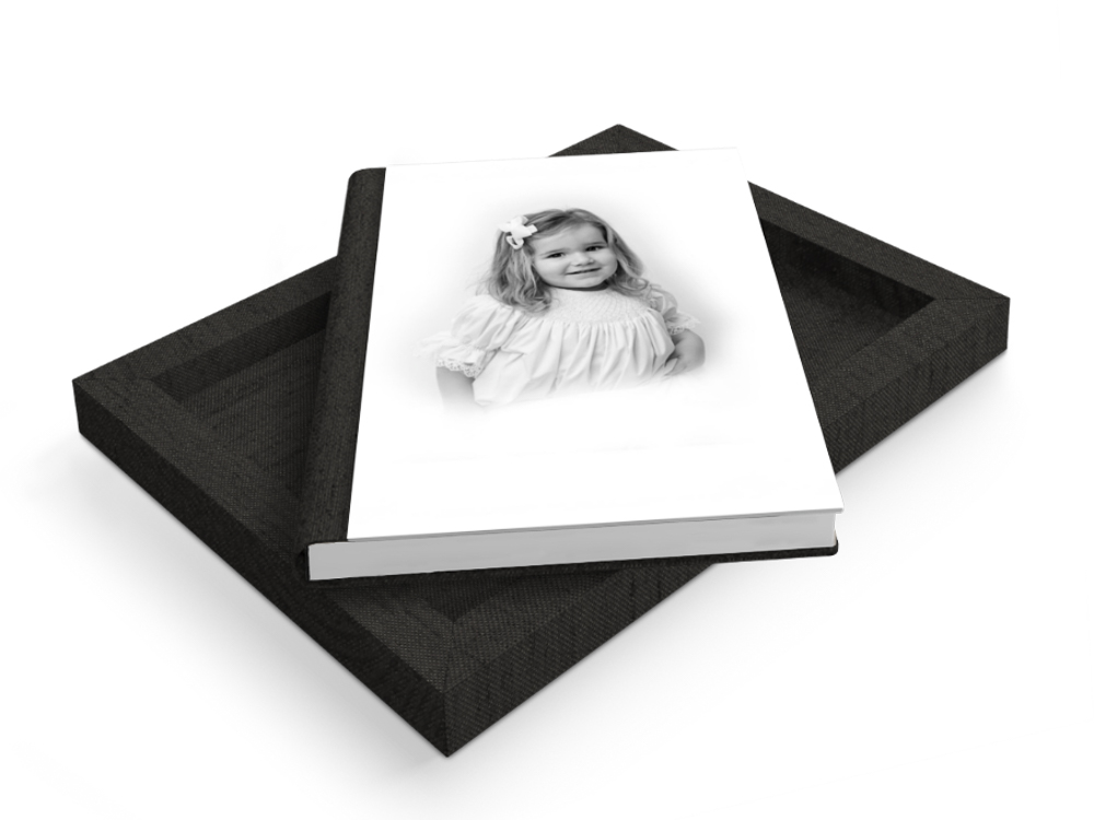 Black linen heirloom album with white pages displaying a black and white portrait of a young child with blonde hair