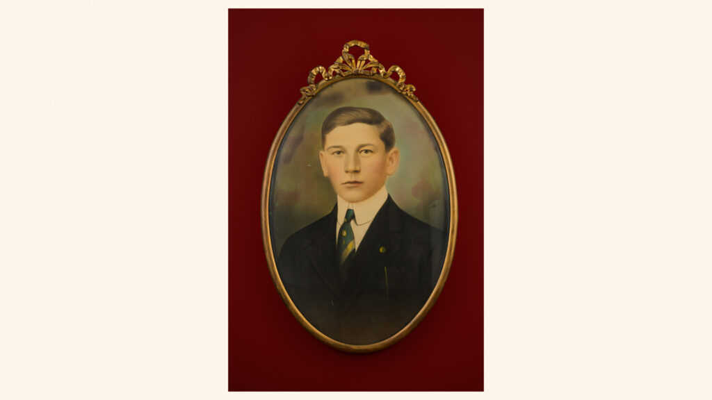 Young man in formal black suit with striped tie in ornate gold oval frame against deep red background